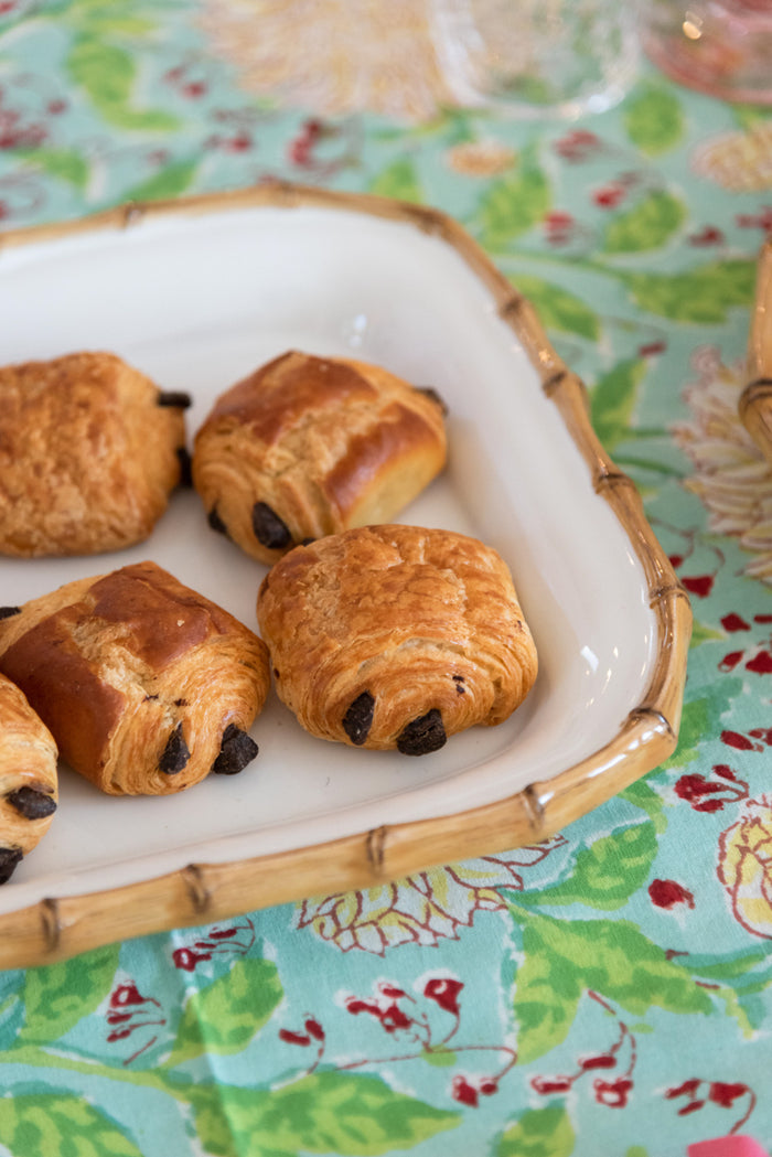 Rectangular bamboo platter with white ceramic inset and croissants on floral tablecloth.