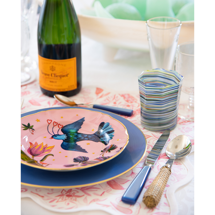Pink dessert plate with floral and hummingbird design, layered on blue dinner plate.