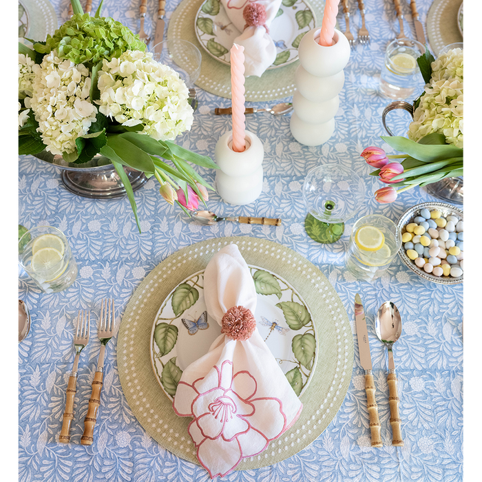 Blue placemat with white dot pattern under plates with green leaf design and floral napkin on decorated dining table.