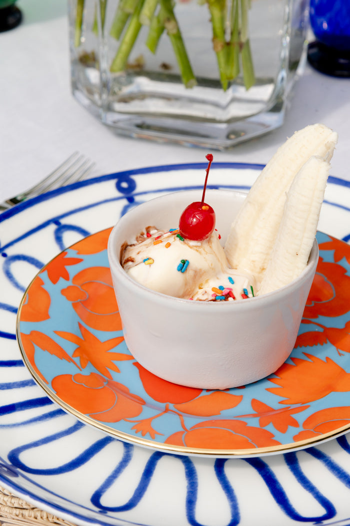 Whitewash ceramic ramekin holding scoops of ice cream with sprinkles and a cherry on top.