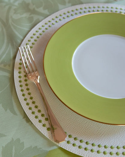 Rose gold dinner fork with a geometric handle resting on layered green and white plates with dotted details.