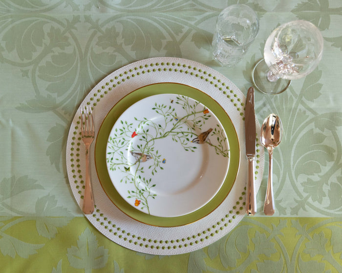 Gold-tone America flatware set with dinner knife, dinner fork, and soup spoon beside floral-patterned plates on green.