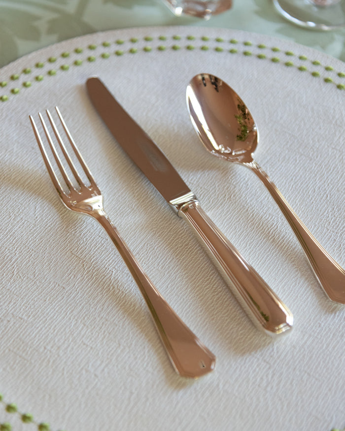 Polished silver flatware set with dinner fork, knife, and spoon on white textured plate.