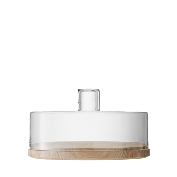 Clear glass dome with cylindrical handle on round light wood base for serving cakes or charcuterie.