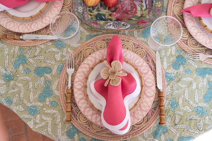 Round natural bamboo cocktail plate with a smaller white ceramic plate and pink cloth napkin topped with a decorative flower .