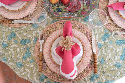 Round natural bamboo cocktail plate with a smaller white ceramic plate and pink cloth napkin topped with a decorative flower .