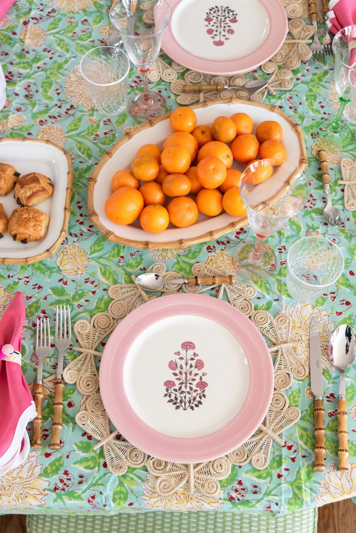 Oval bamboo serving platter filled with small orange kumquats on floral tablecloth.