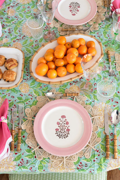 Oval bamboo serving platter filled with small orange kumquats on floral tablecloth.