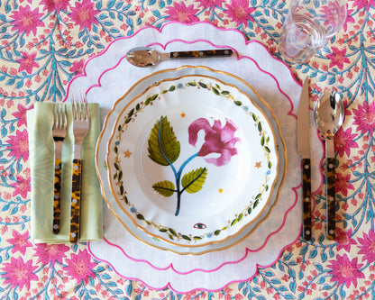 Pink ceramic deep plate with floral design and scalloped edges on patterned tablecloth.