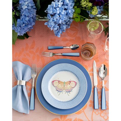 Blue cocktail plate with lace pattern and butterfly accent on white center, paired with blue flatware and napkin on coral.