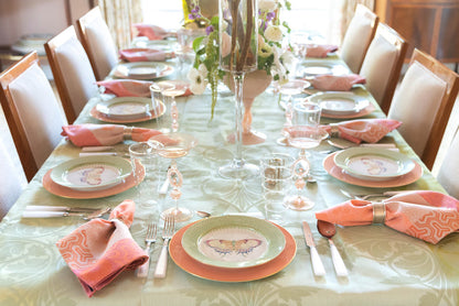 Green apple lace plate with butterfly design set on elegant dining table with pink napkins and glassware.