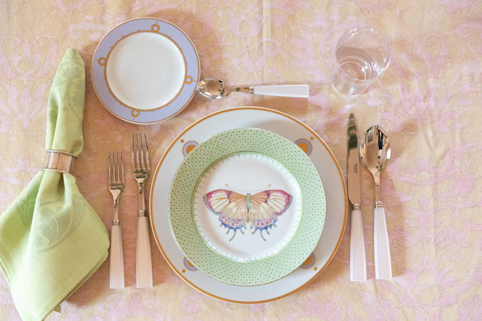 Green apple lace-accented butterfly plate set with gold-rimmed dinnerware and light pink flatware on pink tablecloth.