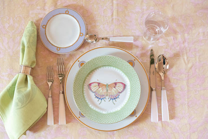 Green apple lace-accented butterfly plate set with gold-rimmed dinnerware and light pink flatware on pink tablecloth.