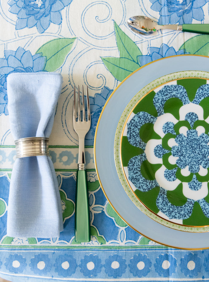 Green apple dessert plate with lace-inspired floral pattern and gold rim on patterned tablecloth.