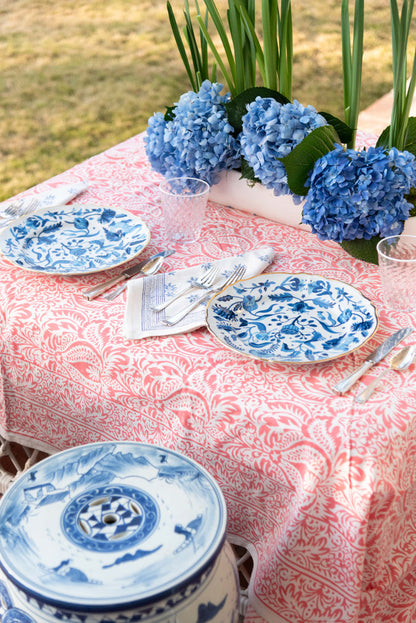 Blue and white ceramic dinner plates with intricate floral and geometric patterns on a pink patterned tablecloth outdoors.
