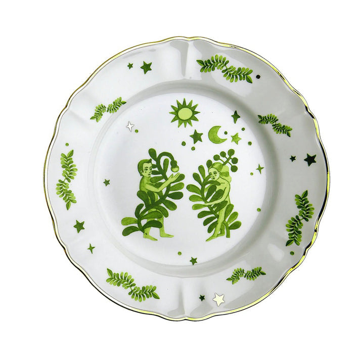 White ceramic dinner plate with scalloped gold-rimmed edge and green botanical and celestial designs.