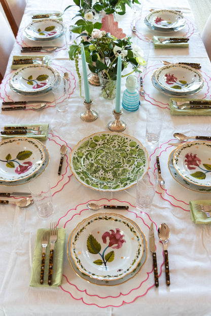 Round ceramic platter with green leafy pattern and wavy pink border on a set dining table.