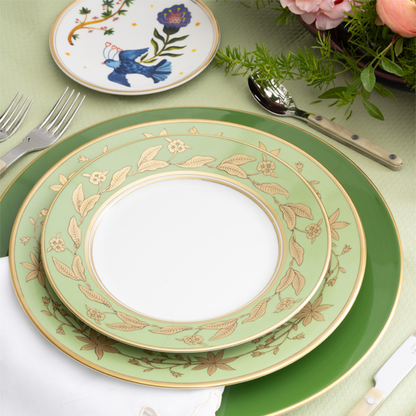 Green ceramic plate with gold floral patterns on a table setting with cutlery and flowers.