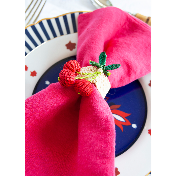 Blue modern geometric dinner plate with red and white floral patterns, paired with a pink cloth napkin and woven fruit.