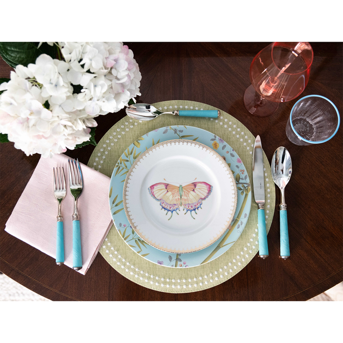 Grass green placemat with white dot pattern under blue and butterfly-themed plates on dark wood table.