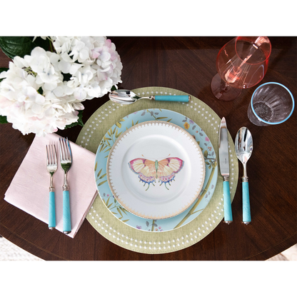 Grass green placemat with white dot pattern under blue and butterfly-themed plates on dark wood table.