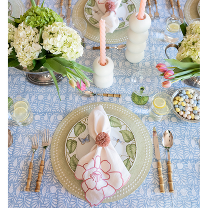 Blue placemat with white dot pattern under plates with green leaf design and floral napkin on decorated dining table.