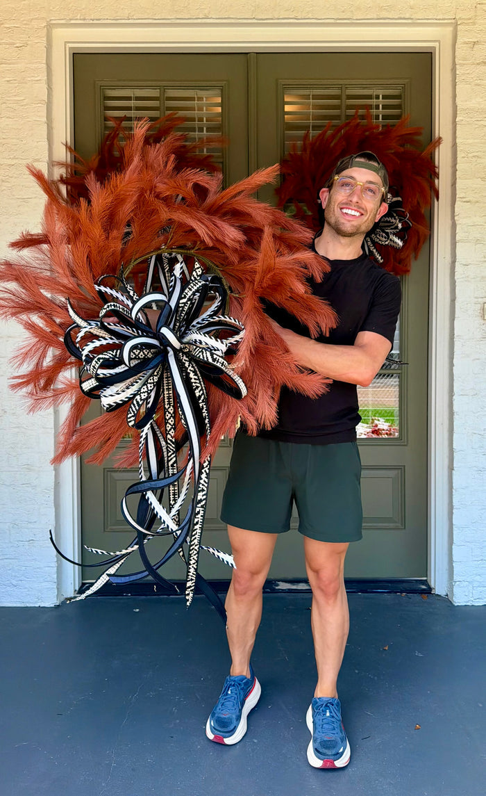 Orange faux plume wreath paired with a hand tied JME bow of black and white 1inch ribbons. About 26 inches in diameter. * some fluffing may be required upon receiving.