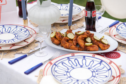 Large white oval ceramic platter with subtle textured finish holding fried chicken pieces, surrounded by blue and red.