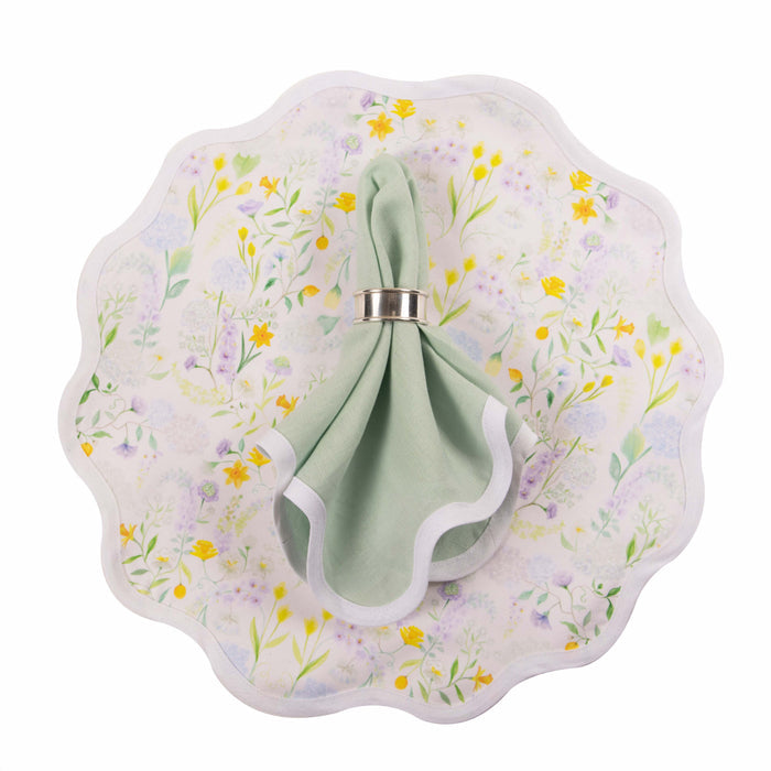 Scalloped linen napkin in sage green with white edge trim on floral patterned plate with yellow and green accents.