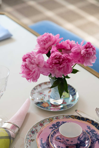 Ceramic bread and butter plate with delicate tobacco leaf pattern under pink flower vase on white tabletop.