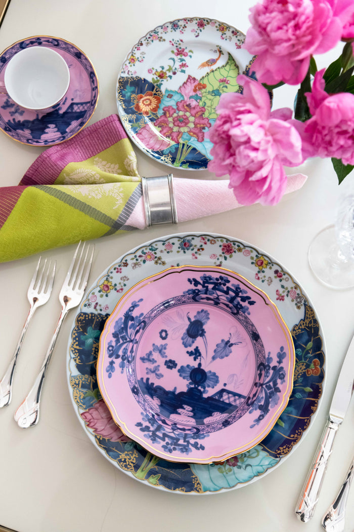 Set of colorful dessert plates with botanical and floral patterns, paired with silver cutlery and pink flowers.