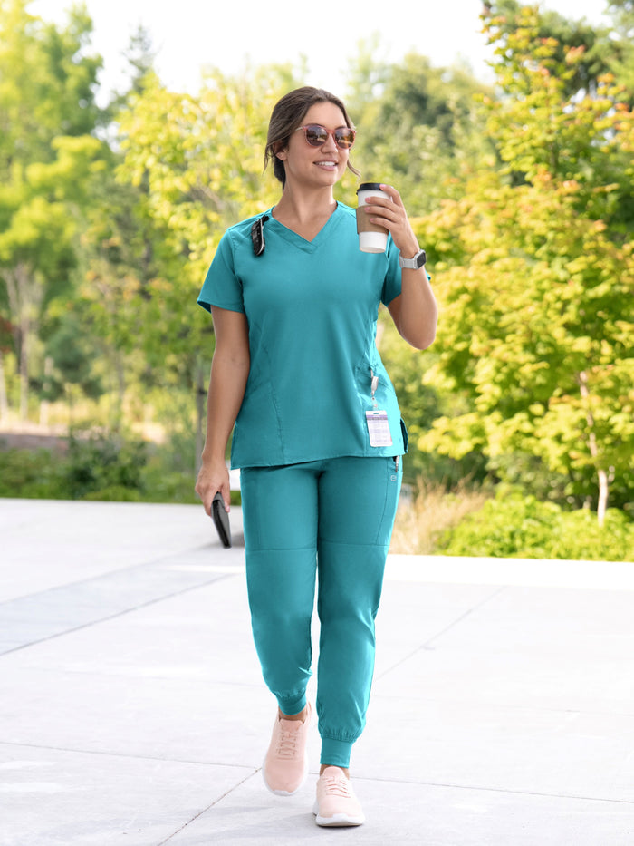 Woman in teal scrubs walking outdoors holding a coffee cup